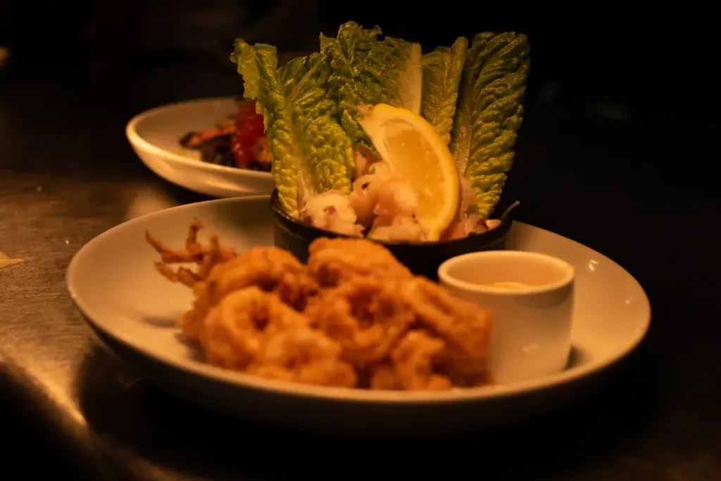 Two plates: fried calamari, seafood salad with lemon, under dim light.