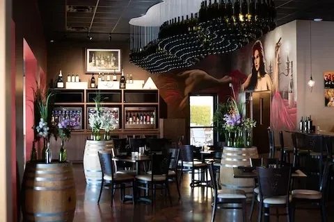 Wine bar interior with barrels, bottle displays, murals, and bottle chandelier.