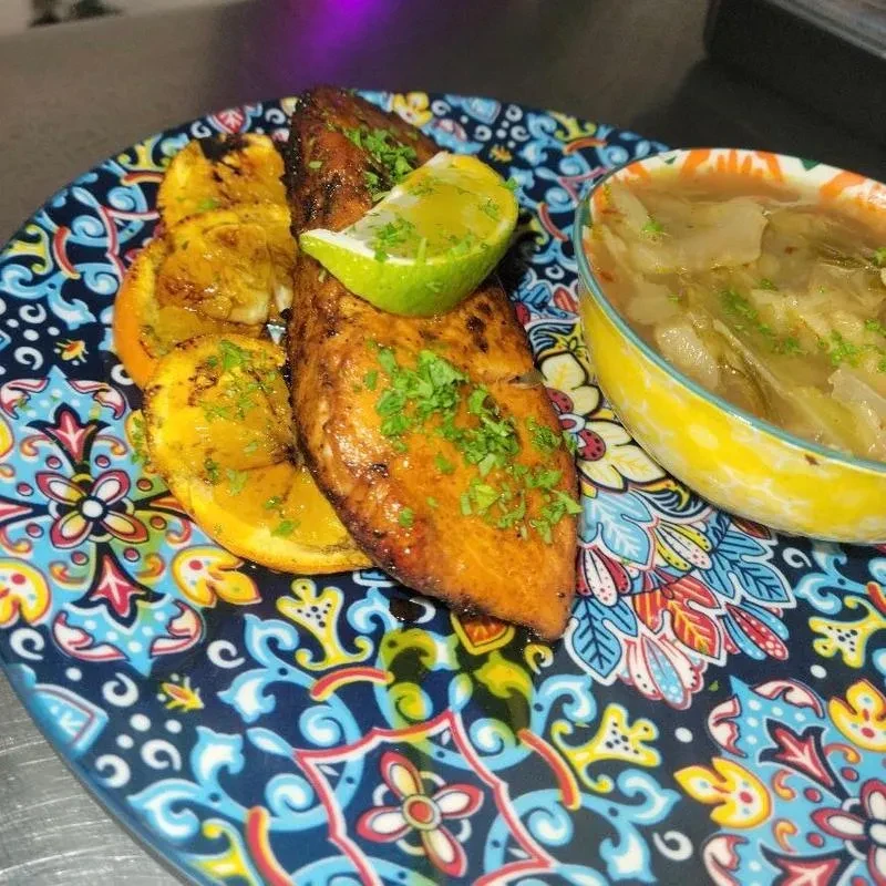 Close-up: Golden fish, orange slices, soup, and decorative floral plate.
