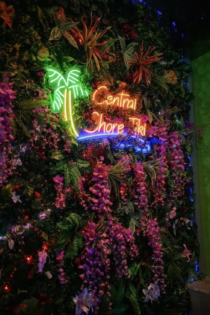 Artificial plant wall with glowing Central Shore Tiki neon sign.