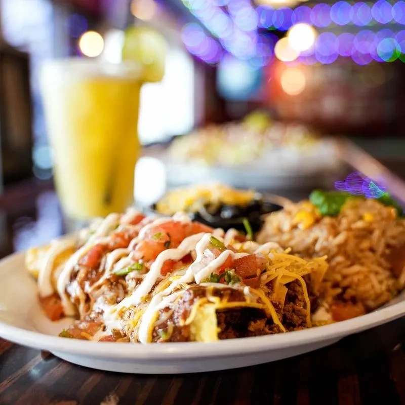 Mexican tacos, rice, beans, and yellow drink on dark wood table.