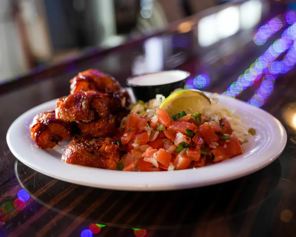 Plate with glazed meat, pico de gallo, sauce, and colorful bokeh.