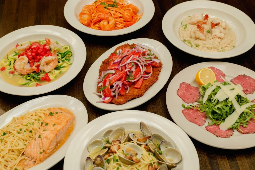 Overhead shot of seven varied pasta, seafood, and meat dishes.