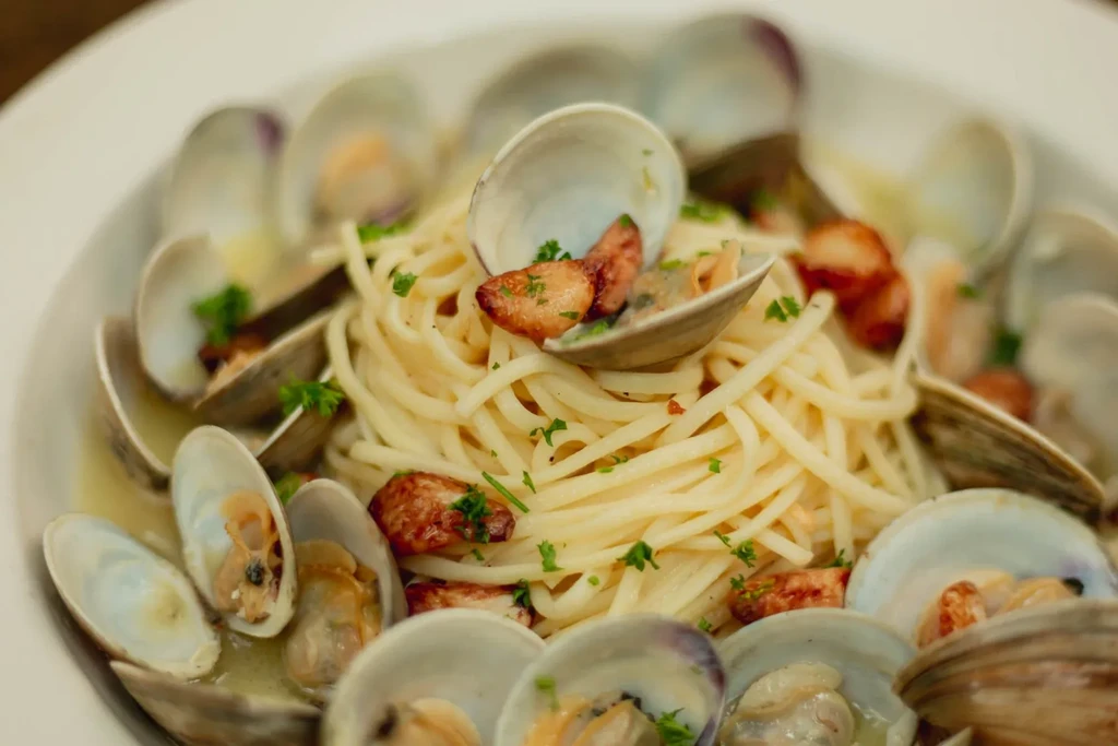 Close-up of spaghetti with open clams, green herbs, and garlic.