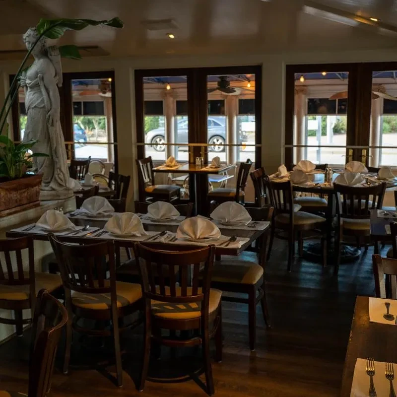Empty formal dining room with set tables, classical statue, natural light.