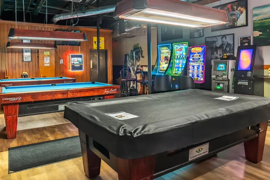An empty pool hall with three tables and brightly lit slot machines.