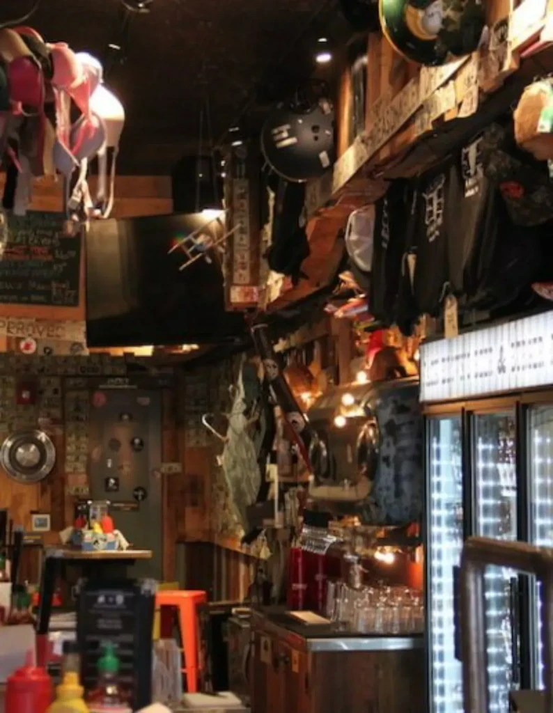 Dimly lit bar interior with eclectic decor, dollar bills, and hanging bras.