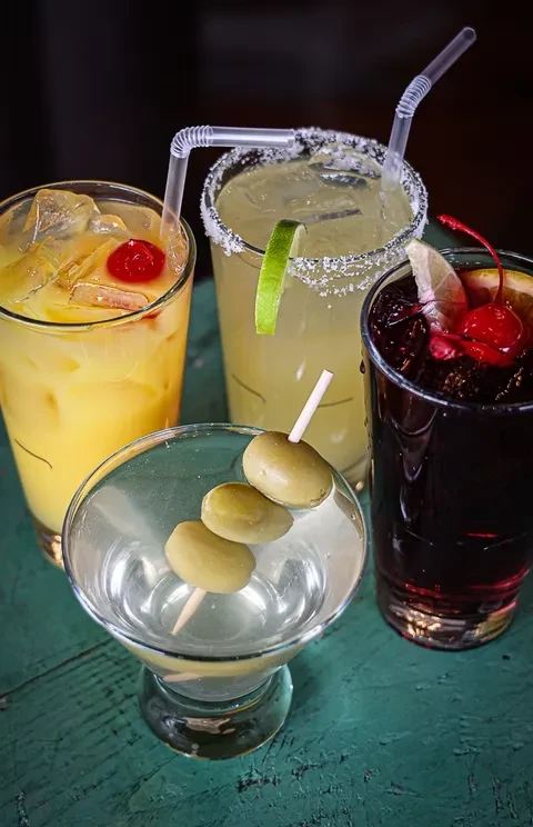 Four distinct garnished cocktails with ice on a teal surface.
