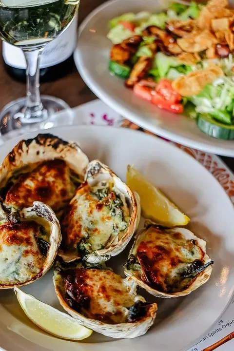 Five baked oysters with melted cheese, herbs, and lemon.
