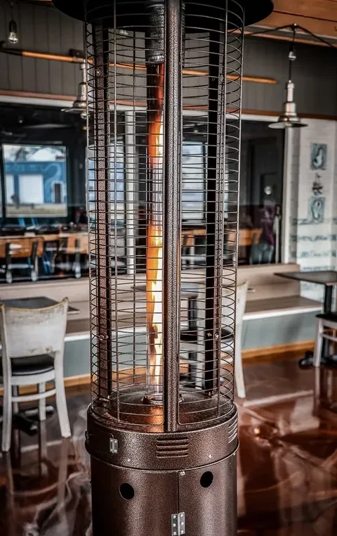 Bronze gas patio heater with a vertical flame in an indoor patio.
