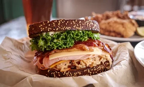 Multi-layered club sandwich on dark seeded bread with bacon and chicken.