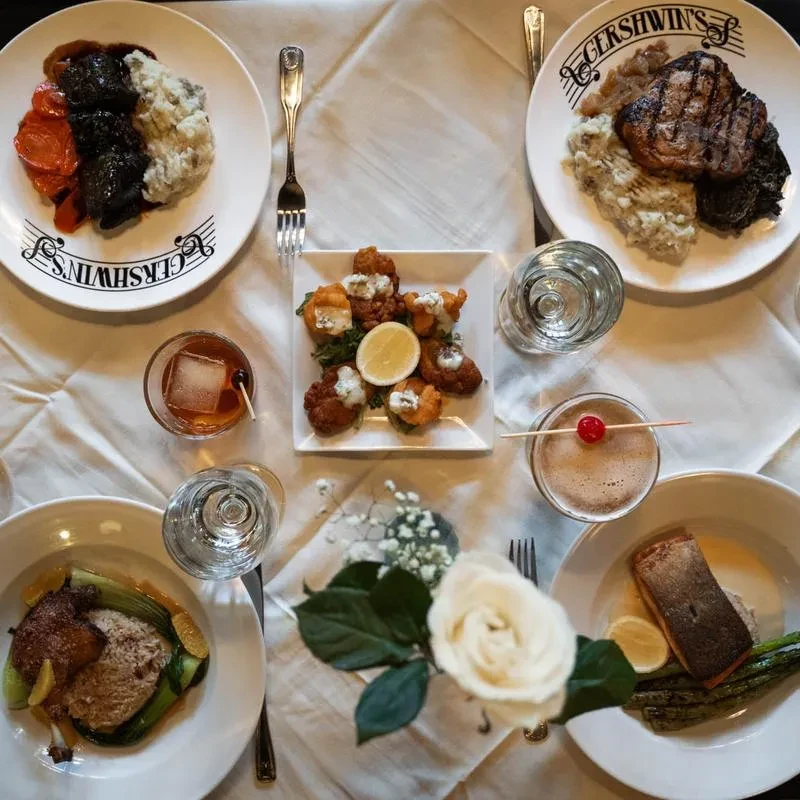 Upscale dining table overhead, set with gourmet food, drinks, and a rose.