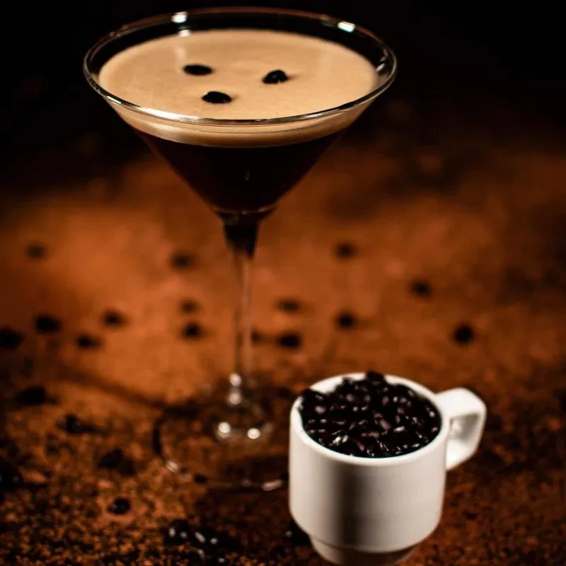 Martini glass with coffee foam and beans, alongside overflowing coffee cup.