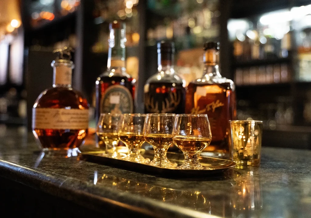 Gold tray with five whisky tasting glasses and blurred spirit bottles.