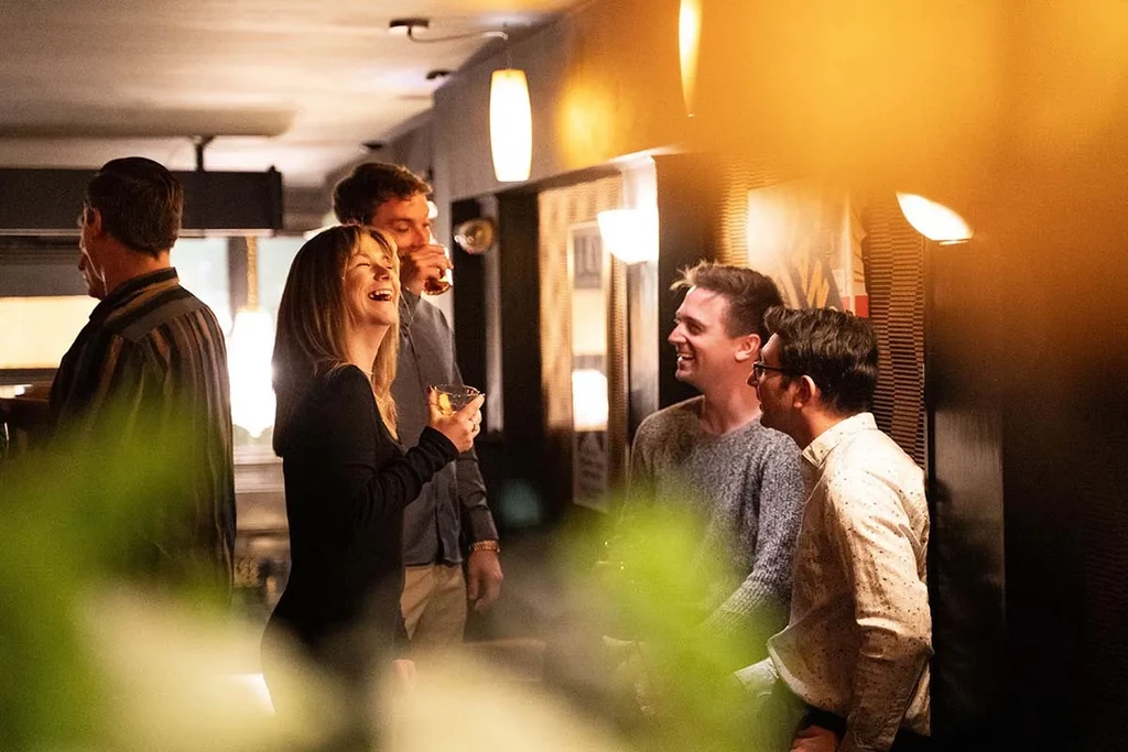 Friends laughing and drinking in a warm, lively restaurant.