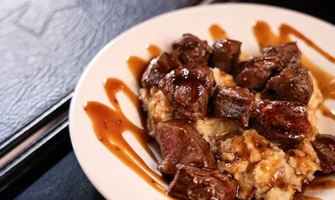 Diced seared meat in glossy brown sauce over creamy base.
