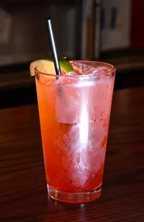 Iced reddish-orange cocktail garnished with lime and a straw.