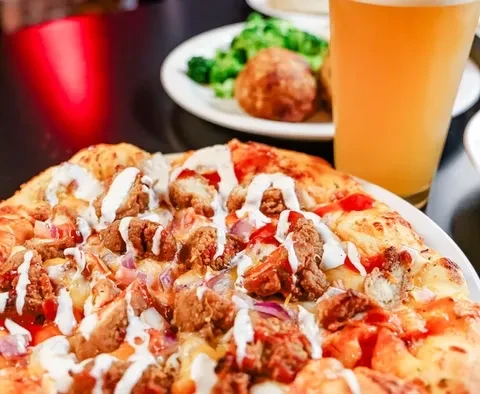 Gourmet chicken pizza with red onions, white sauce, and beer.