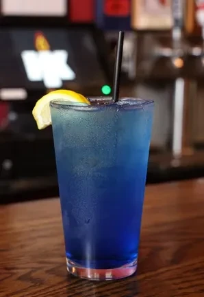 Blue drink with lemon, straw, and ice on a wooden bar.