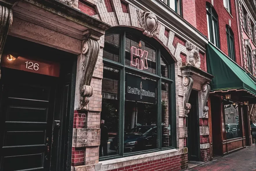 Historic brick Hell's Kitchen storefront with ornate details and glowing red neon sign.
