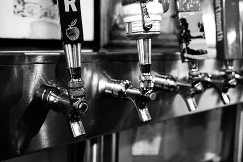 Black and white photo of four beverage taps on a bar.