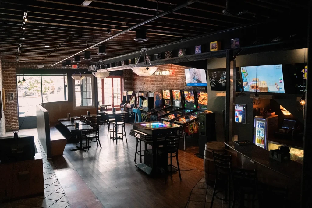 Arcade bar interior with glowing games, dining area, and bar.