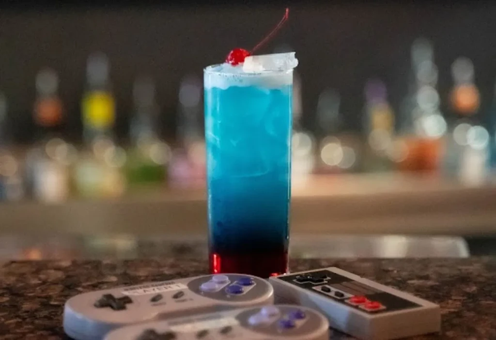 Layered blue and red cocktail with cherry, two vintage game controllers.