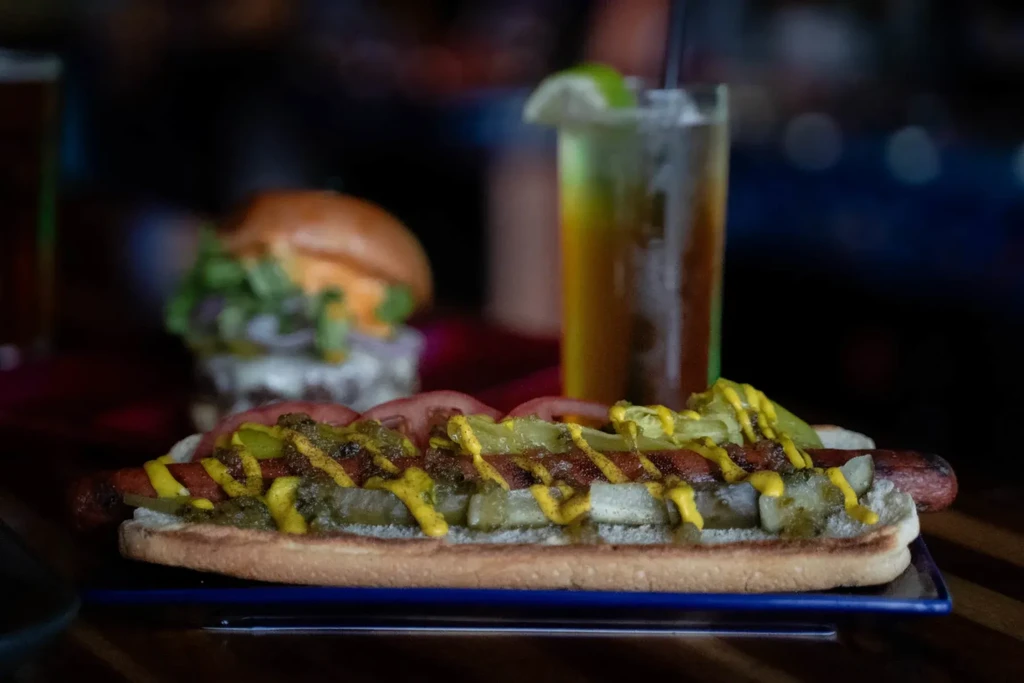 Close-up of a loaded hot dog with mustard, pickles, relish, and tomatoes.