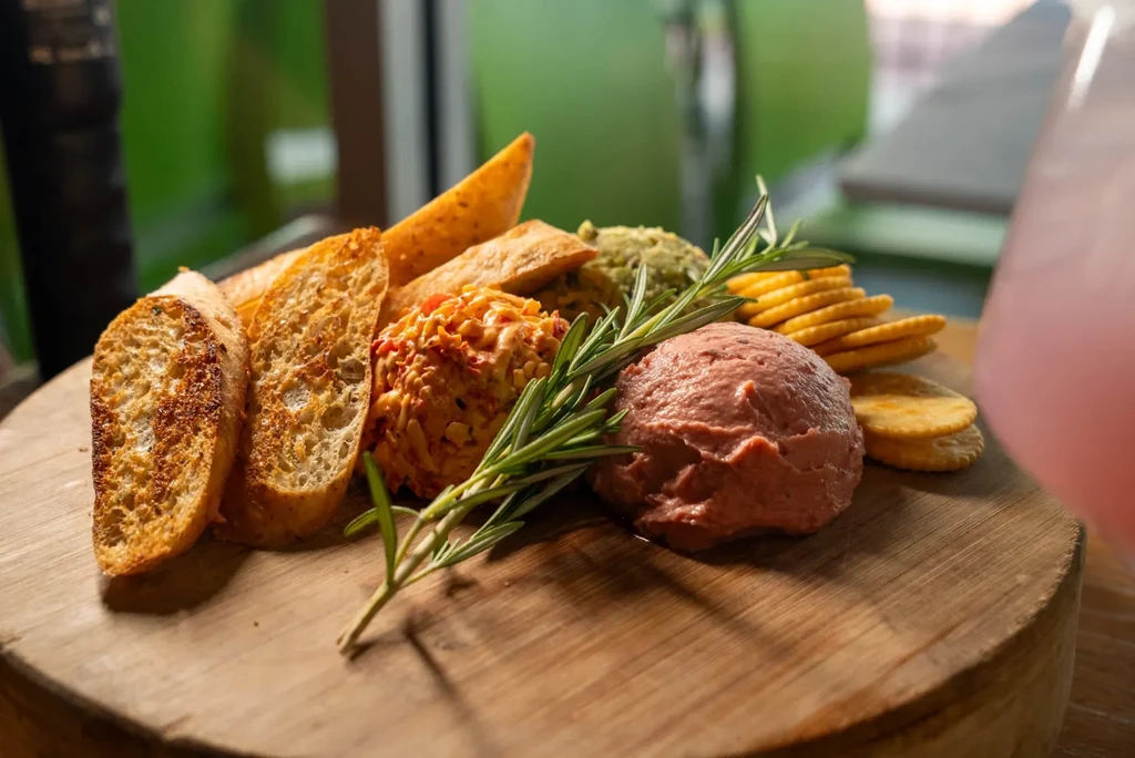 Appetizer platter of spreads, rosemary, baguette, crackers on wooden board.