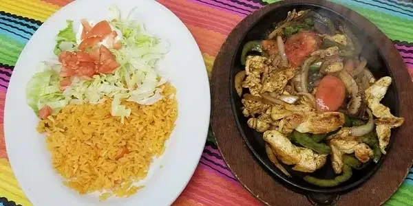 Sizzling chicken fajitas and Mexican rice on a colorful striped tablecloth.