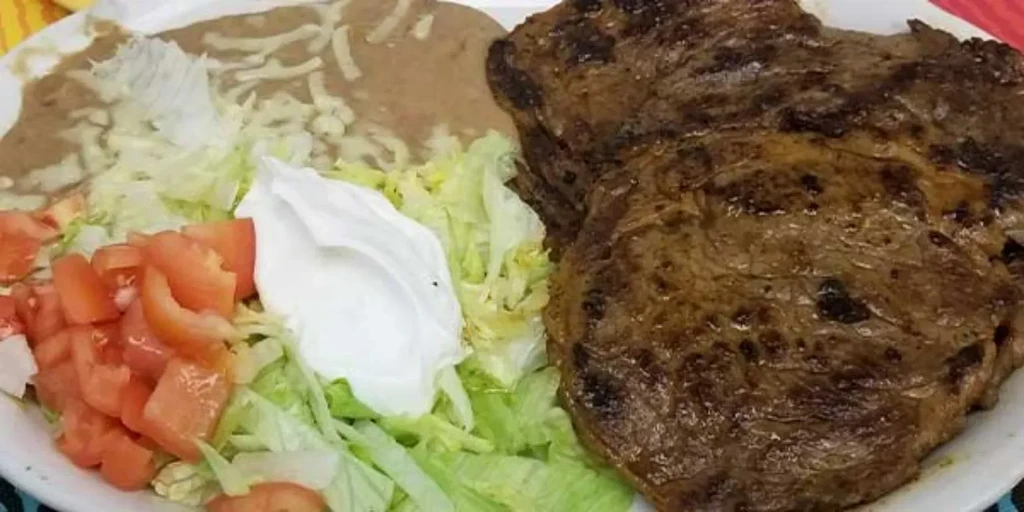 Plated grilled steak, refried beans, lettuce, tomatoes, and sour cream.