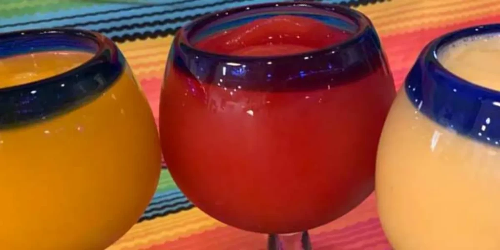 Vibrant red and yellow-orange drinks in Mexican glasses on a serape.