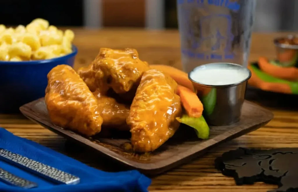Glistening buffalo wings with crudités and dipping sauce on a wooden plate.