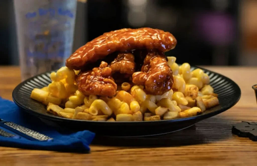 Mac and cheese, crispy fries, and sauced fried chicken on a dark plate.