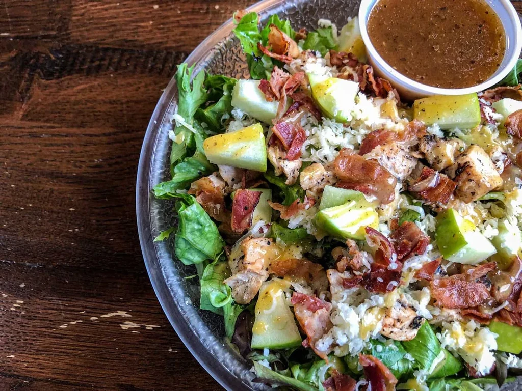 Overhead: Salad with grilled chicken, bacon, apple, cheese, and dressing.
