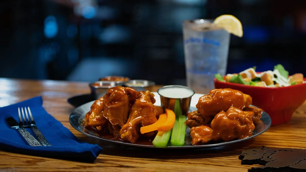 Plate of buffalo wings, celery, dressing, and salad on a wooden table.