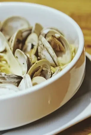 White bowl of cooked clams with pasta or broth on a table.
