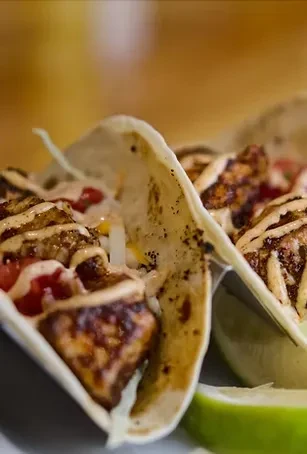 Two gourmet tacos filled with seasoned protein, tomatoes, sauce, and lime.