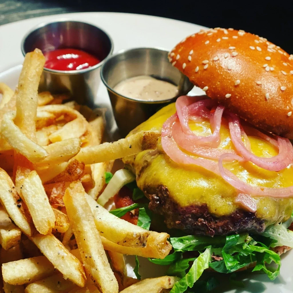 A cheeseburger with melted cheese, red onions, fries, and sauces.