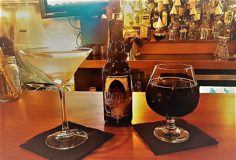 Wooden bar top with martini, "DARK HOLLOW" bottle, and snifter.