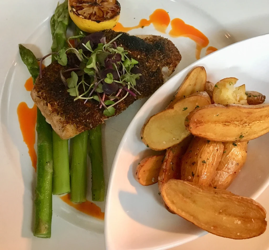 Seared fish with microgreens, asparagus, roasted potatoes, and charred lemon.