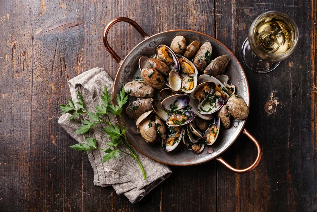 Rustic meal: cooked clams in pot, wine, parsley on wooden table.