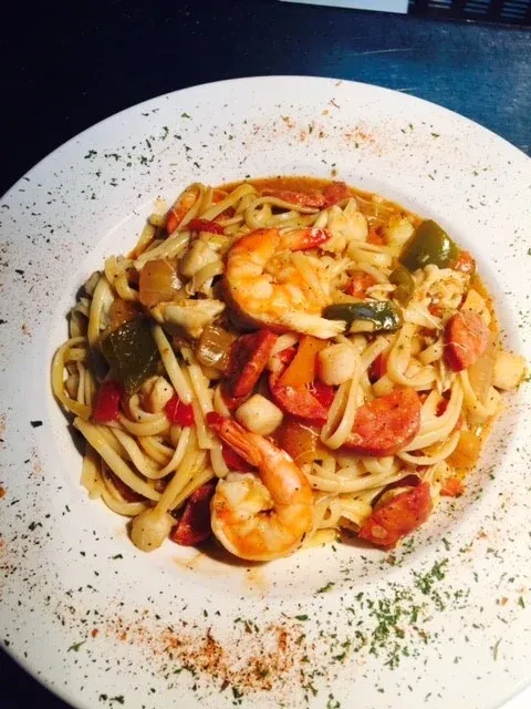 Close-up of shrimp and sausage seafood pasta with reddish-orange sauce.