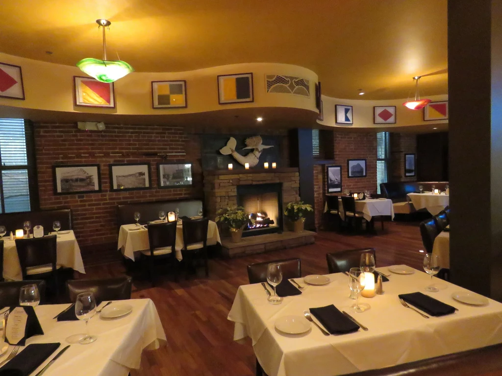 Cozy restaurant dining room with fireplace, mermaid sculpture, and signal flags.