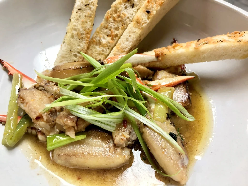 Close-up of shellfish in sauce with green vegetables and toasted bread.