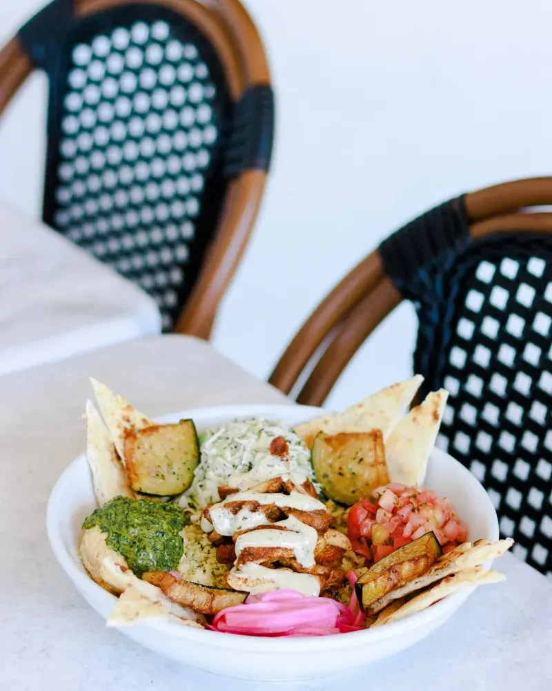 Vibrant Mediterranean chicken bowl with pita, sauces, and fresh vegetables.