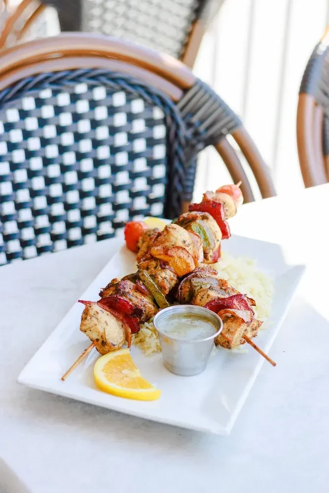 Grilled chicken skewers, peppers, onions, rice, sauce, lemon on plate.