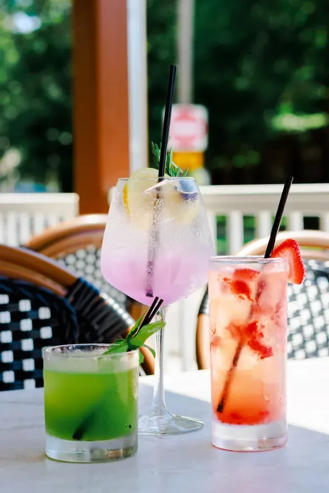 Three colorful, garnished cocktails on an outdoor restaurant patio table.
