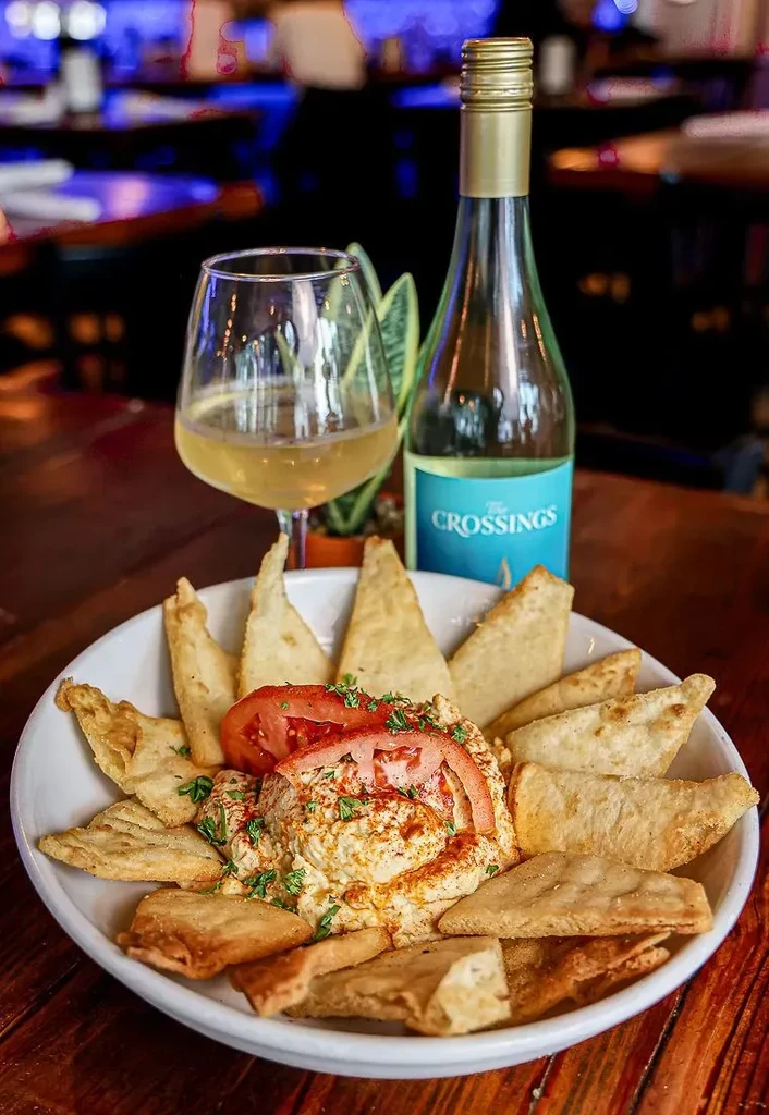 Hummus, pita bread, and The CROSSINGS white wine on wooden table.
