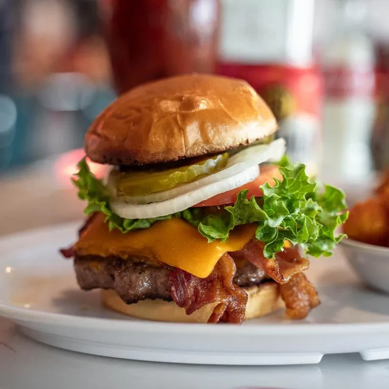 Close-up gourmet cheeseburger with bacon, cheddar, lettuce, tomato, onion, pickles.